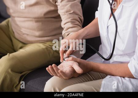 cropped view of social worker examining aged man with stethoscope on blurred background Stock Photo