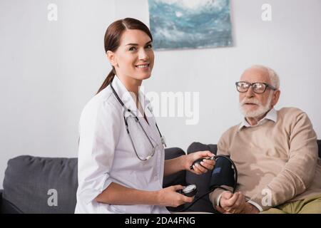 smiling social worker looking at camera while checking health of patient with stethoscope Stock Photo