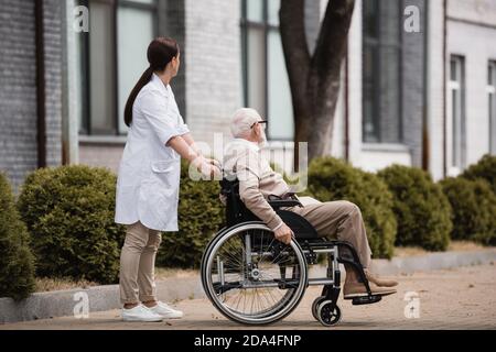 social worker walking with aged disabled man on wheelchair outdoors Stock Photo