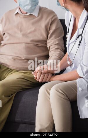 cropped view of nurse checking health by holding hands with aged patient Stock Photo