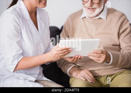 cropped view of geriatric nurse showing digital tablet to aged man on blurred background Stock Photo