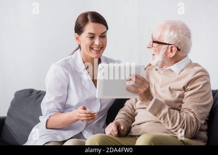 happy aged man showing digital tablet to excited social worker Stock Photo