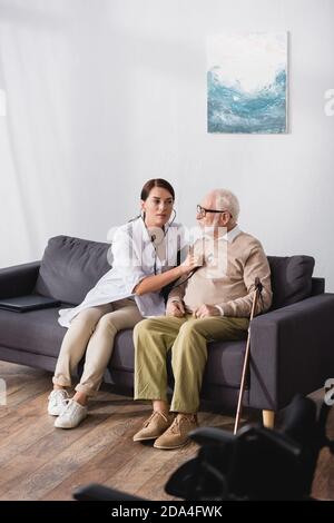 geriatric nurse checking heath of aged man with stethoscope Stock Photo