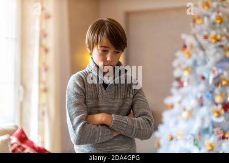 Unhappy boy standing by Christmas tree Stock Photo