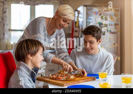 Mother and sons eating pizza for lunch at home Stock Photo