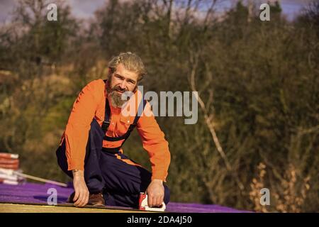 Roof installation. Bearded man work outdoor. Roof Mechanic concept. Inspect repair and replace. Assemble temporary equipment or structures. Structural sheathing. Fix or build. Roofer repair roof. Stock Photo