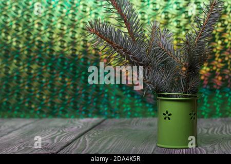 Branches of blue spruce in a decorative bucket. On brushed pine boards painted black and white. The background is an iridescent surface of green. Stock Photo