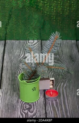 Branches of blue spruce in a decorative bucket. Nearby is a candle. On brushed pine boards painted black and white. Stock Photo