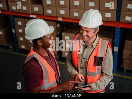 Two colleagues smiling while discussing business plans holding digital tablet standing in warehouse  Stock Photo