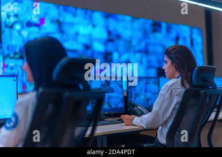 Group of Security data center operators (administrators) working in a group at a CCTV monitoring room while looking at multiple monitors ( computer sc Stock Photo