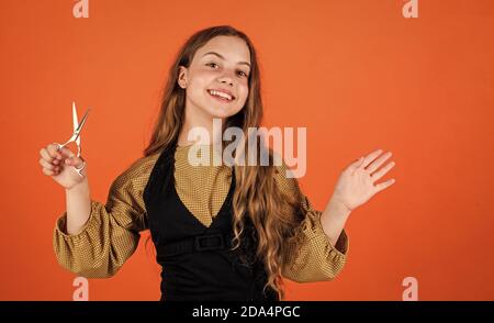 child with scissors wants to cut hair. girl in hairdressing salon. teenager cutting hair. Cute girl cutting hair to herself with scissors. kid is trimmed in the hairdressers. Form follows you. Stock Photo