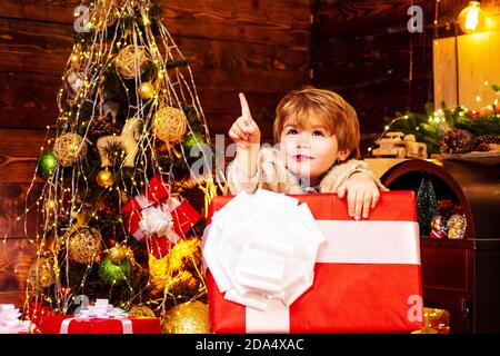 New year concept. Winter kid. Christmas children. Child with big gift box. Winter Christmas emotion. Child with a Christmas present on wooden house Stock Photo