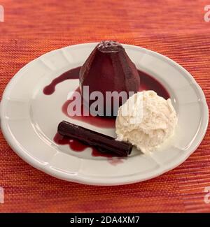 Pear stewed in red wine, with wine sauce, cinnamon stick and vanilla ice-cream over white plate Stock Photo