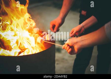 Human hands holding sticks for open fire marshmallow roasting at night time. Close view background with place for text Stock Photo