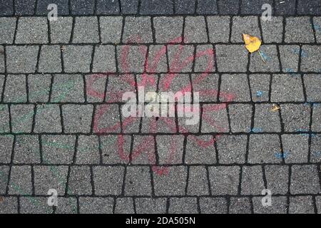 Children's chalk drawing washed away by autumn rain on paving stones and alone yellow birch leaf. Cobblestone street in city. Paved boulevard or avenu Stock Photo