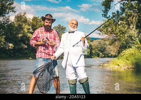 Generations ages: grandfather and father. Grandfather and boy fishing together. Happy grandfather and grandson with fishing rods on river berth. Stock Photo