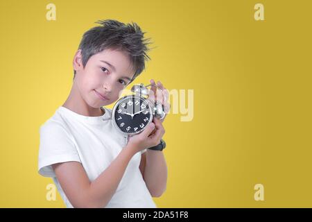 School boy with alarm clock in hands isolated on yellow. Time to go Stock Photo