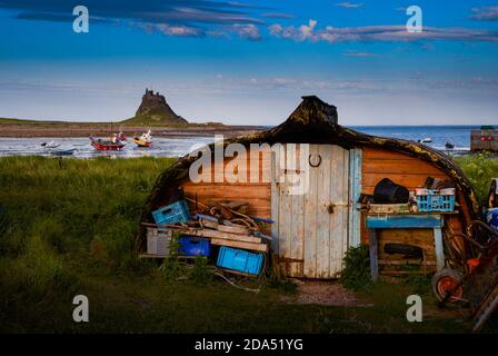 Lindisfarne Castle on Holy Island, Northumberland, England viewed from the harbour where old herring boats are used as fishermen's sheds. Stock Photo