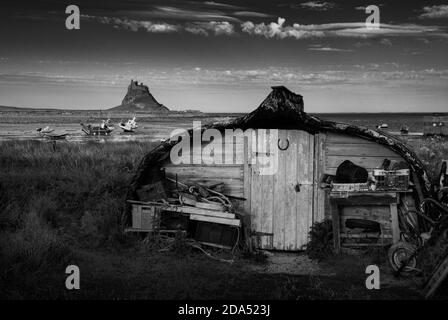 Lindisfarne Castle on Holy Island, Northumberland, England viewed from the harbour where old herring boats are used as fishermen's sheds. Stock Photo