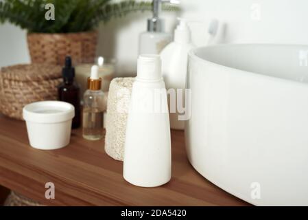 Light-colored bathroom sink with tubes of cream, jars of facial serums and clean towels. The concept of skin care, daily washing and cleanliness. Stock Photo