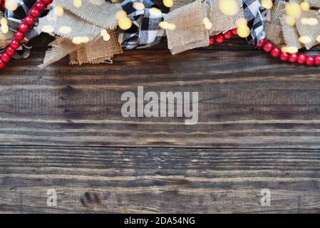 Christmas garland with bokeh lights, burlap, black and white buffalo check fabric and a string of red beads over rust wood table background. Top view Stock Photo