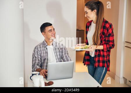 Smiling wife serving breakfast to her freelancer husband Stock Photo