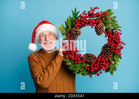 Portrait of his he nice attractive cheerful cheery bearded grey-haired Santa father holding in hands decor December green wreath celebratory day
