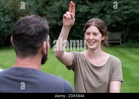 Therapist and client seated in a garden, woman with her hand raised and two fingers extended. Stock Photo