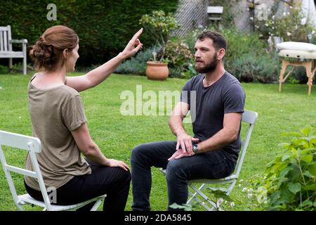 Therapist and client seated in a garden, woman with her hand raised and two fingers extended. Stock Photo