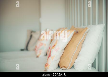 Side view of a bright neat made bed with rows of pillows and multicolored cushions on the top leaning against a wooden striped bulkhead, shallow depth Stock Photo