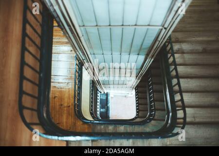 View from above with a shallow depth of field of a long stairwell going down in a spiral, an old residential building with a metal railing and a lift Stock Photo