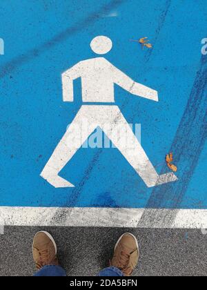 Photo of Feet in Sport Shoes Standing by Blue Walking Sign on the Road Stock Photo