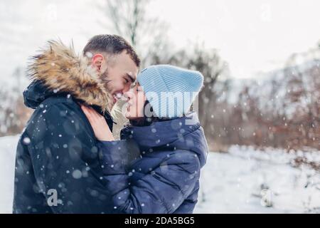 Man and woman kissing and hugging in winter forest. Couple enjoying snowfall outdoors Stock Photo