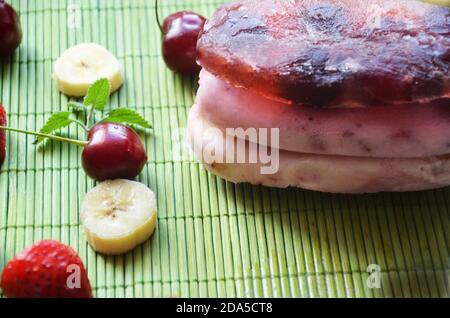 Homemade strawberry cherry banana blueberry ice cream or popsicles decorated green mint leaves on teal rustic table, frozen fruit juice, vintage style Stock Photo