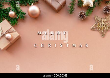 Festive Christmas background with spruce twigs, gift box and baubles on beige table with words Merry Christmas. Top view Stock Photo