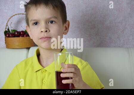 Cute little boy drinking juice at home, cherry juice drinks from a bottle or a glass with a straw Stock Photo