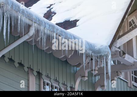 Ice stalactite hanging from the roof with wooden wall. Building covered with large icicles Stock Photo