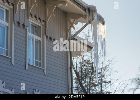 Ice stalactite hanging from the roof with wooden wall. Building covered with large icicles. Stock Photo