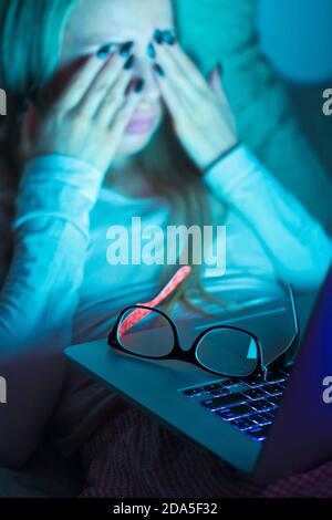 Young woman with glasses rubbing her eyes, feels tired after working on laptop, lying in bed on pillow. Overwork, Exhausted, fatigue. Stock Photo