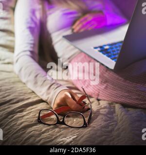 Woman with glasses holding in hand, fall asleep after working at night on laptop computer, focus on glasses. Sleep, overtime working concept Stock Photo