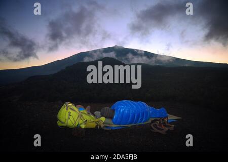 alone hiker is sleeping in blue bag on volcanic ashes in Etna Park, Sicily Stock Photo