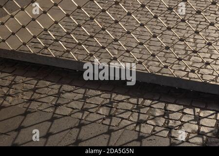 Low angle view of closed air flowable Roller shutter Grille with grid tessellation pattern . Golden Sunlight cast shadow of Grille on ground. Stock Photo