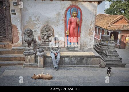 Kathmandu, Nepal, March 2009. A man looks at dogs sitting next to a Buddha statue in a square behind the Swayambhunath Stupa. Stock Photo