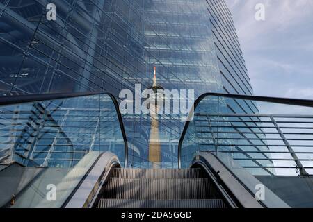 Exterior, low angle view from escalator with background of reflecting Rheinturm, Rhine tower, on glass building's facade of Stadttor tower. Stock Photo
