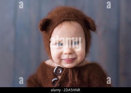 Happy little boy in a brown, fluffy, knitted bear costume, sits on the furon the wooden floor, plays with a bright Christmas garland of lights. Stock Photo