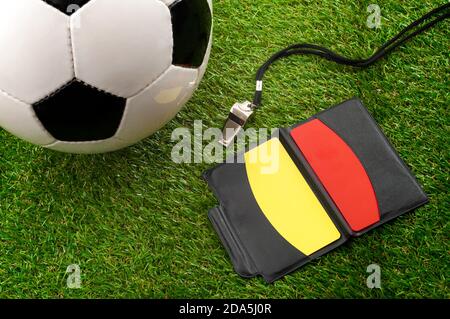 Team sports, rules official gear and athletics competition conceptual idea with soccer ball, yellow and red referee cards and metal whistle on green s Stock Photo