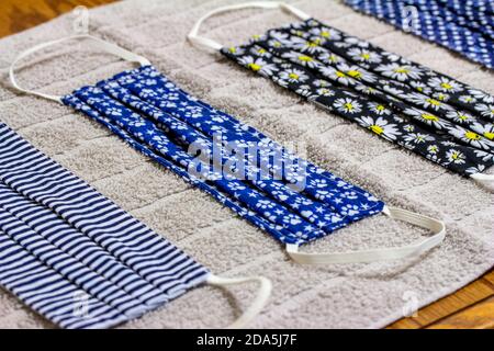 Close up view of four various print hand-washed COVID protective face masks, drying on a cotton towel on kitchen table Stock Photo