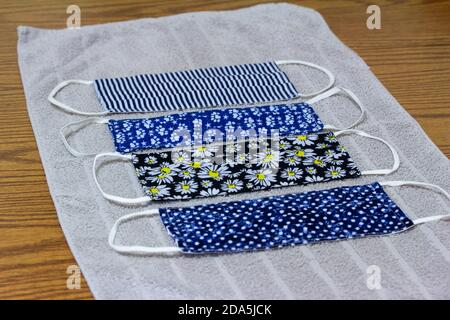 Close up view of four various print hand-washed COVID protective face masks, drying on a cotton towel on kitchen table Stock Photo