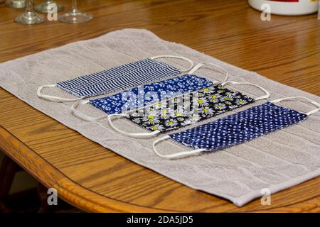 Close up view of four various print hand-washed COVID protective face masks, drying on a cotton towel on kitchen table Stock Photo