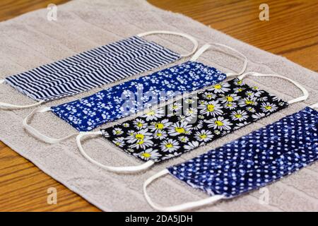 Close up view of four various print hand-washed COVID protective face masks, drying on a cotton towel on kitchen table Stock Photo